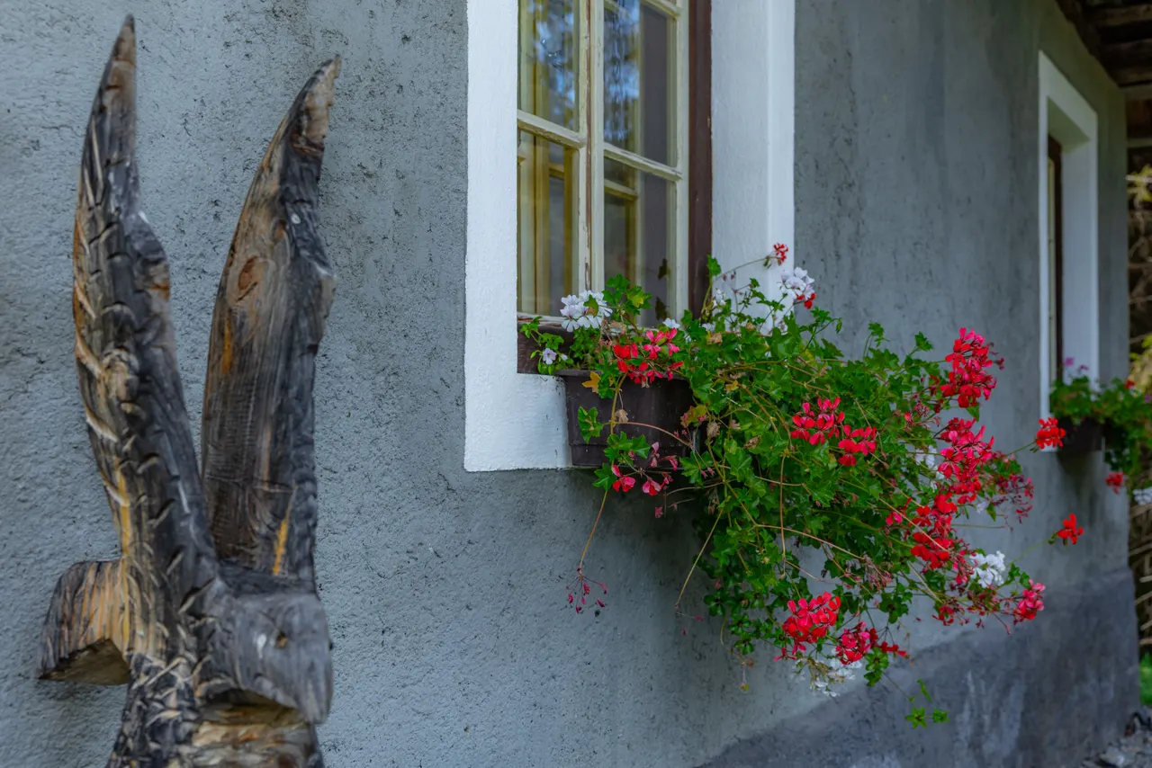 Rote Geranien am Fenster neben einer geschnitzten Holzfigur