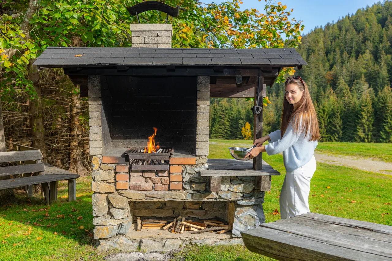 Der gemauerte Grill mit brennendem Feuer, daneben eine junge Frau mit einer Schüssel