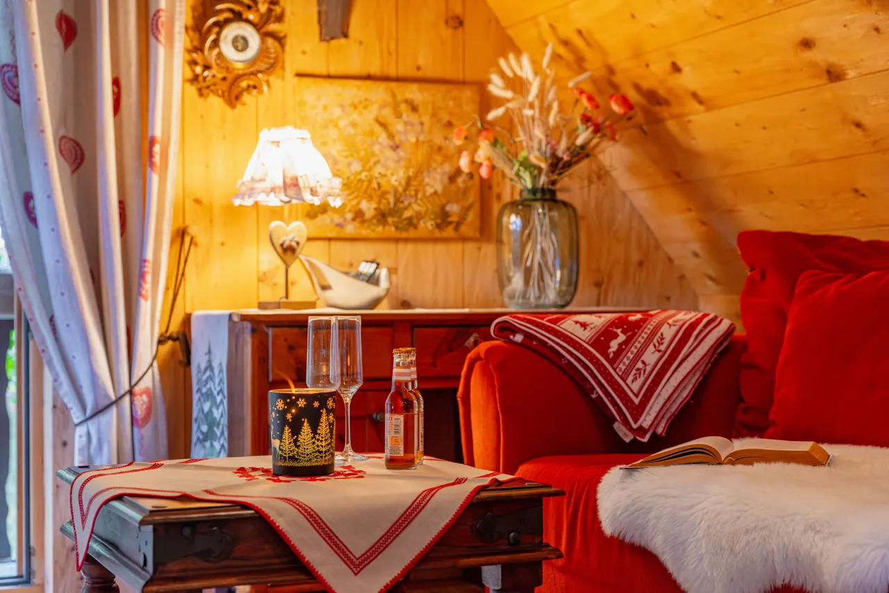 Eine Ecke im Dachgeschoss: Lampe, Windlicht, zwei Gläser und ein aufgeschlagenes Buch auf dem roten Sofa