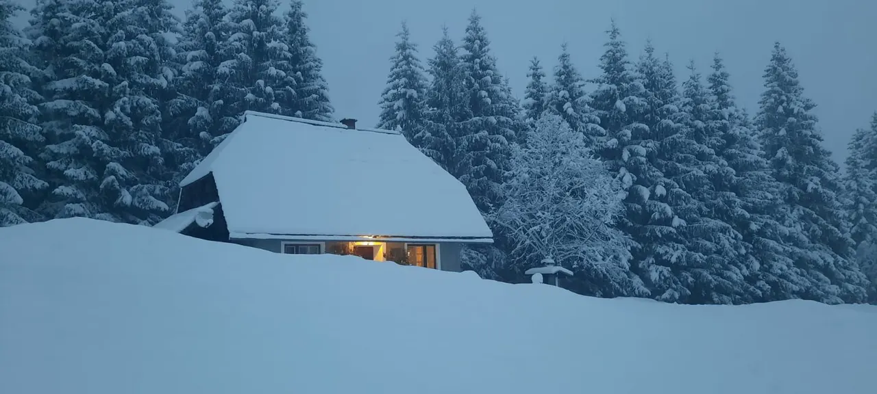 Die Droneberger Hütte in der Abenddämmerung, fast im Schnee vergraben, ein Fenster leuchtet